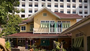 A two-story building with a balcony, a covered patio, and a garden area with chairs and tables. - Panida Suite (Bangkok)
