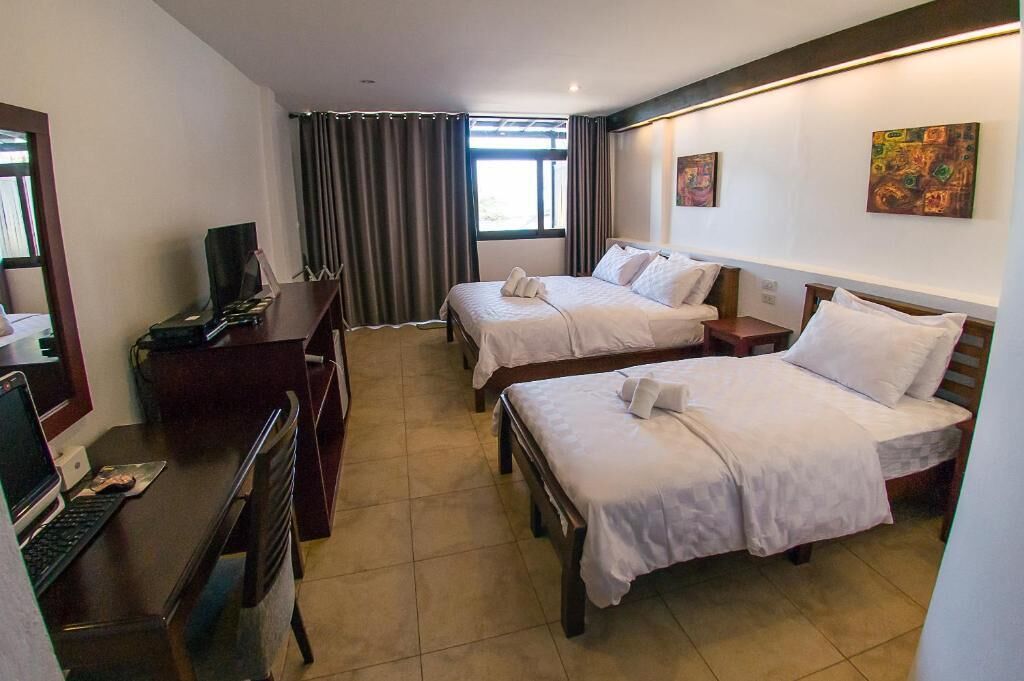 Una habitación de hotel con dos camas, un escritorio con una computadora, un televisor y una ventana con cortinas.
