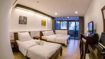 A hotel room with two single beds, a desk with a computer, and a large window with a view of palm trees.