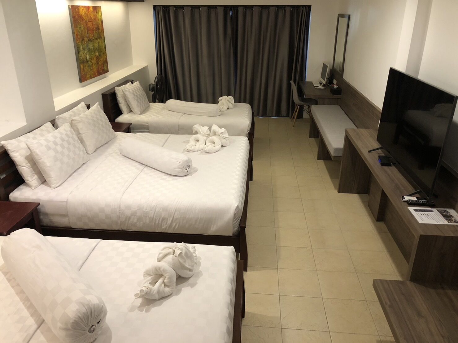 Habitació d'hotel amb tres llits, televisió i escriptori.