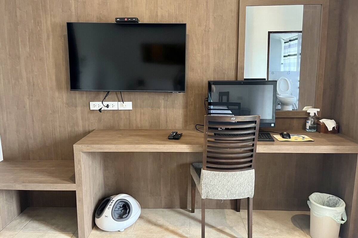 Habitación de hotel con escritorio de madera, televisor, computadora, silla, lavadora y basurero.