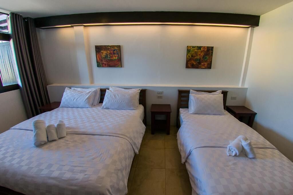 A hotel room with two beds, each with a pillow and a rolled towel. There are two small nightstands between the beds.