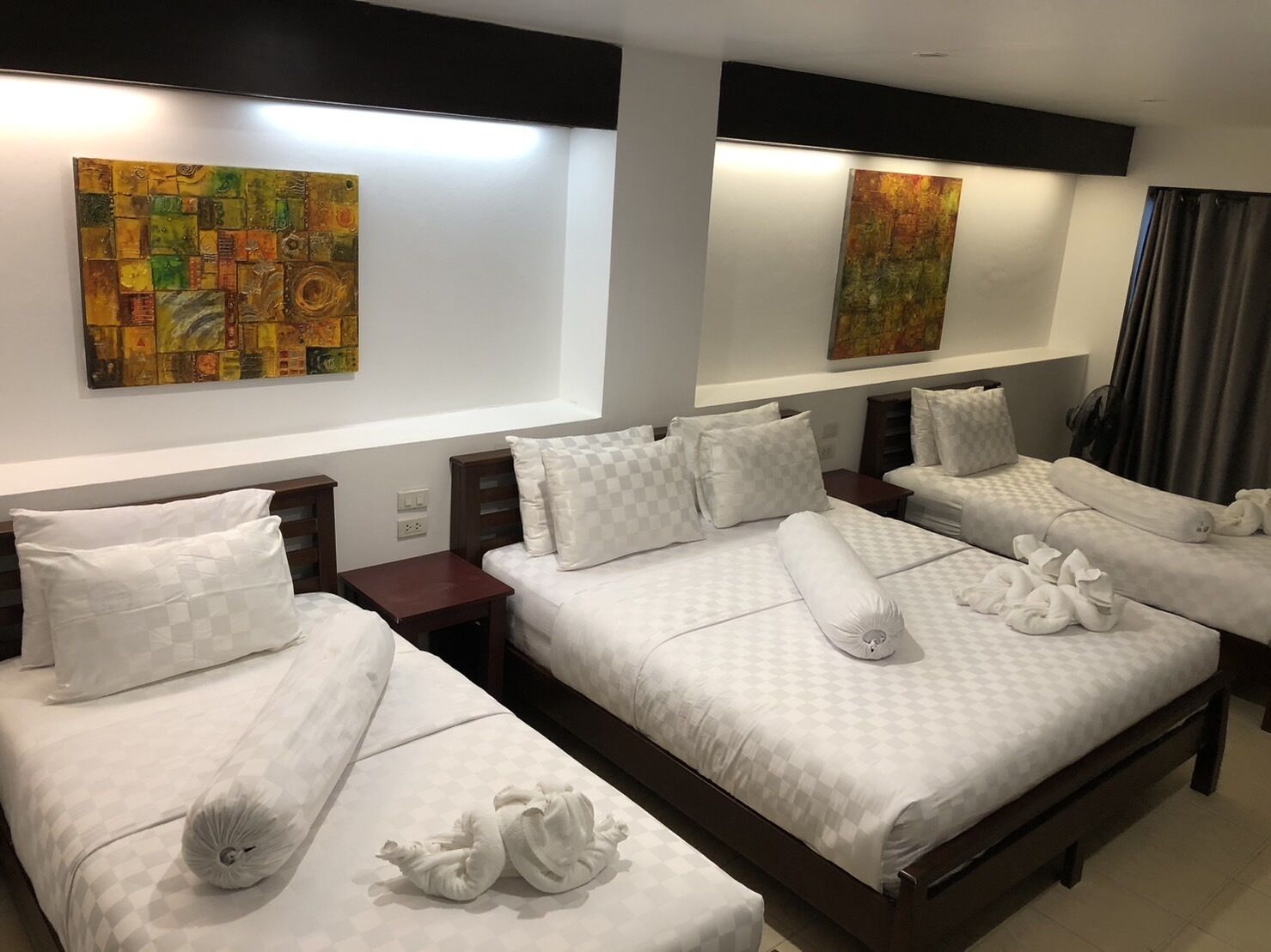 Habitación de hotel con dos camas, cada una con almohada a cuadros y una toalla. Hay cuadros abstractos en las paredes y una ventana con cortinas.