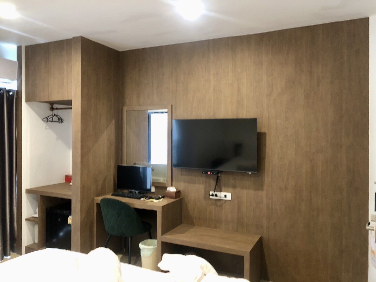 Una habitación de hotel moderna con un revestimiento de madera, un televisor de pantalla plana montado sobre un escritorio, una silla y una cama con ropa blanca.