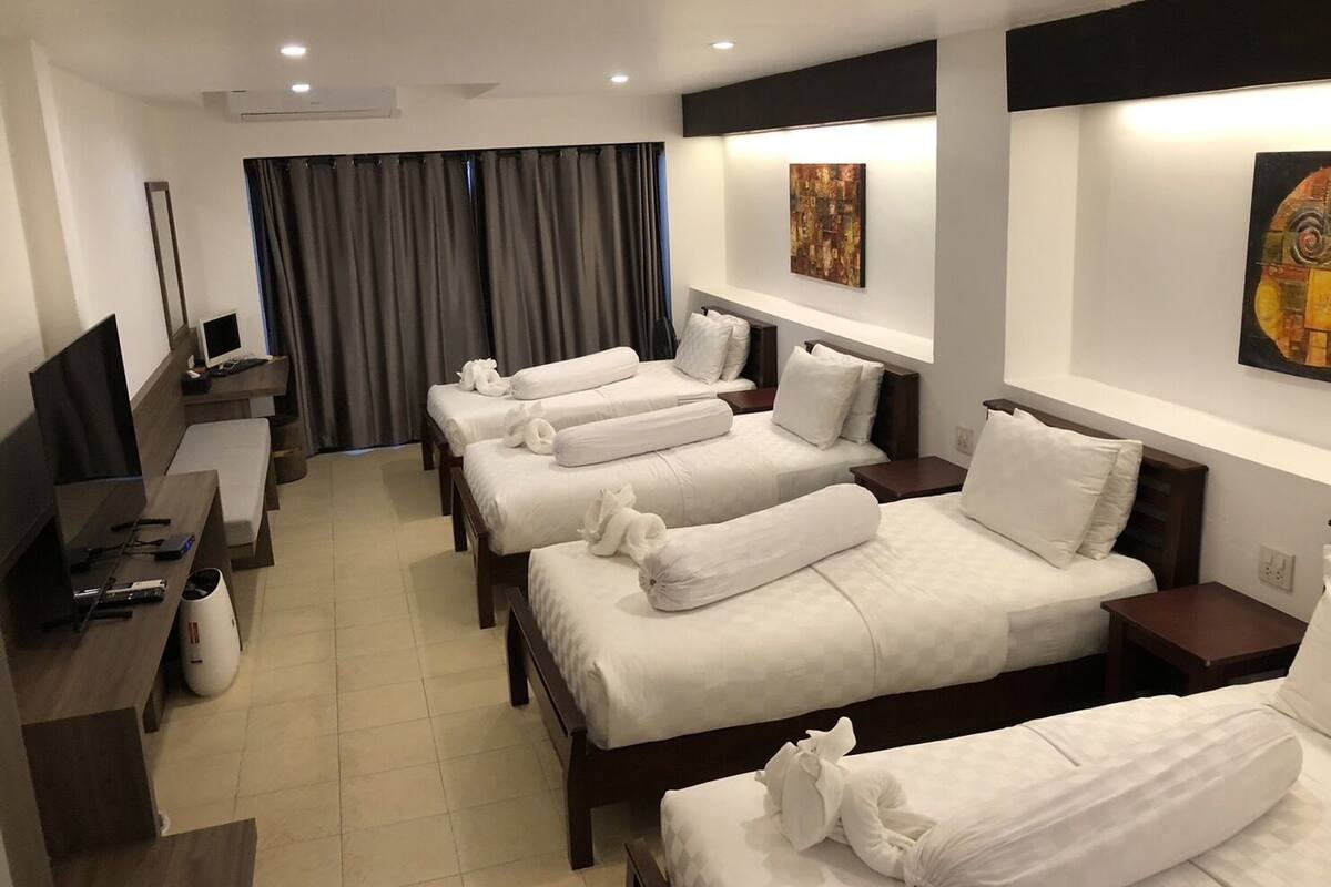 Una habitación de hotel con cuatro camas individuales, un escritorio con computadora y una televisión.