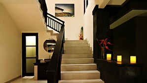 A staircase with a black railing, a wall-mounted picture, and three lit candles on a dark surface. - Gili Pearl Villa (Gili Trawangan)