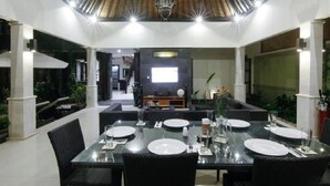 An indoor dining area with a glass table set for four, surrounded by black wicker chairs. - Gili Pearl Villa (Gili Trawangan)