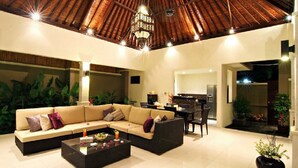 A spacious living area with a large sofa, a coffee table, and a dining table. There is a kitchen area visible in the background. - Gili Pearl Villa (Gili Trawangan)