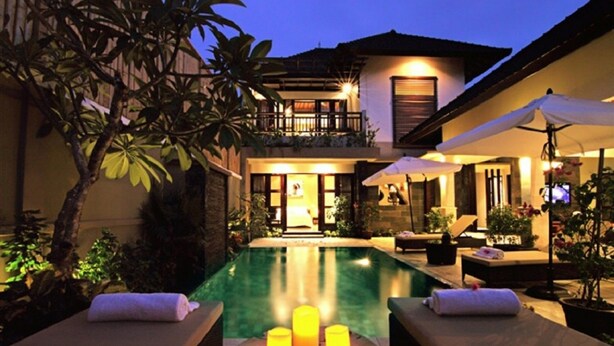 A poolside area with lounge chairs, candles, and a building with a balcony in the background. - Gili Pearl Villa (Gili Trawangan)