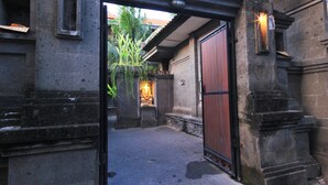 A stone entrance with a wooden door, a small shrine with a statue, and a potted plant. - Letos Kubu Homestay (Kuta)
