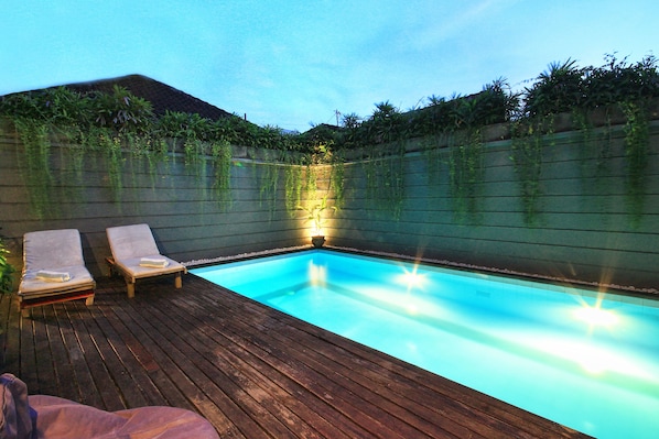 A swimming pool with two lounge chairs and a wooden deck.