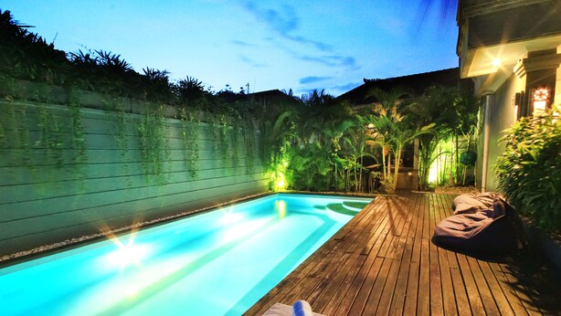 A swimming pool with a wooden deck, a towel, and a water feature. - Letos Kubu Homestay (Kuta)