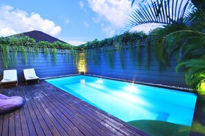 A swimming pool with a wooden deck, two lounge chairs, and a wall covered in greenery. - Letos Kubu Homestay (Kuta)