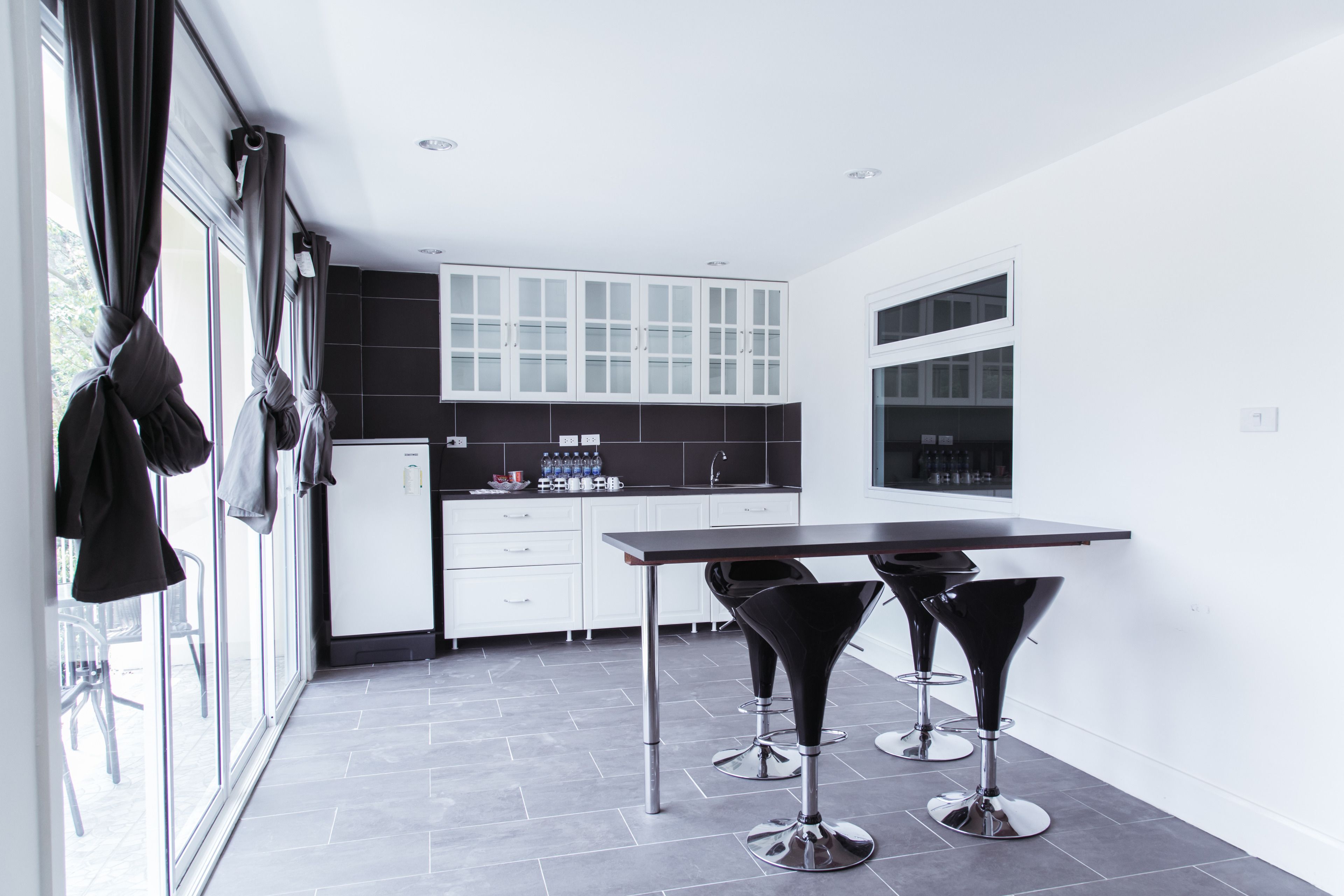 A modern kitchen with white cabinets, a black countertop, and two black bar stools.