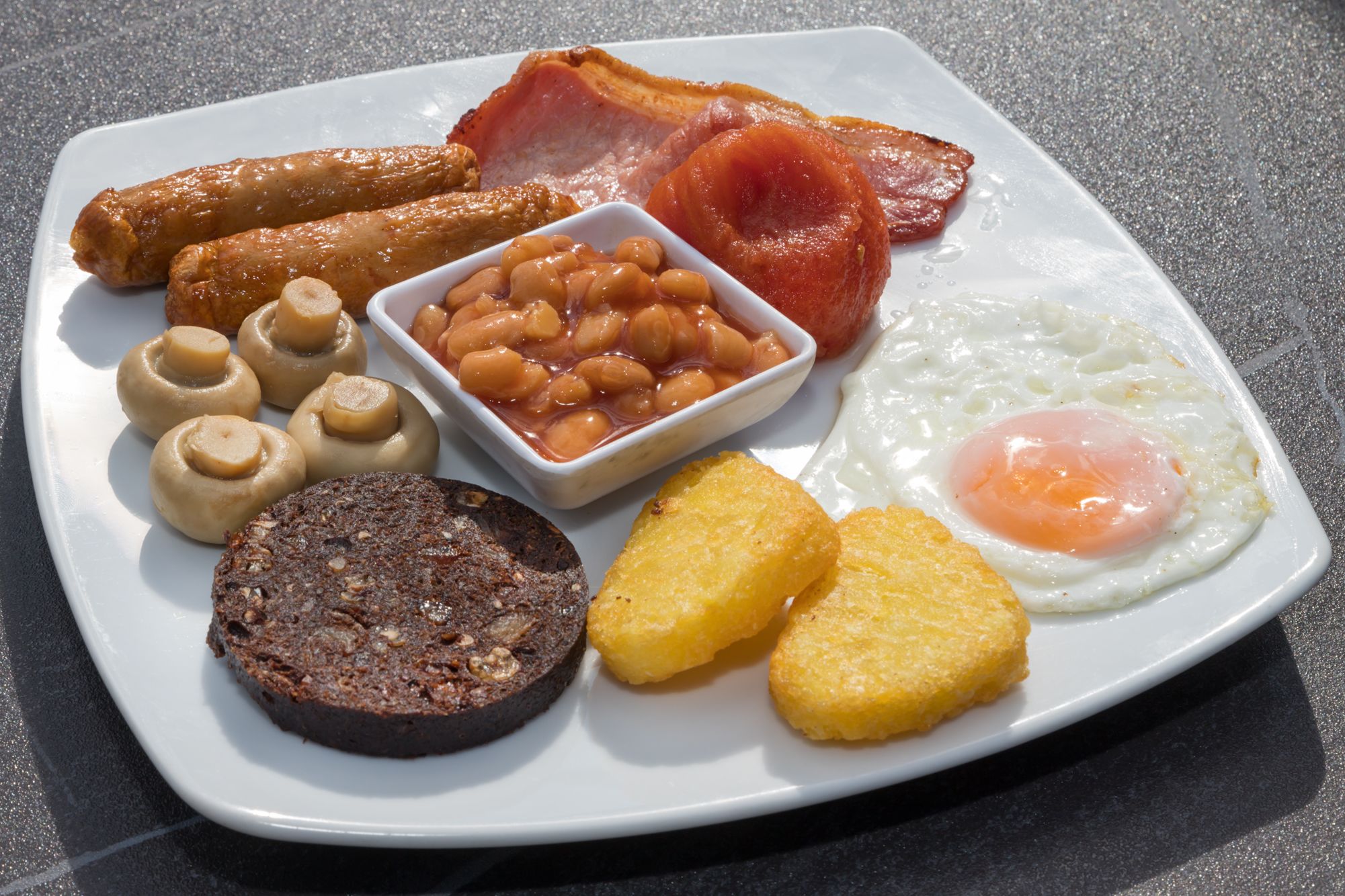 Un plato de desayuno con tocino, salchichas, huevos, frijoles y tostadas.