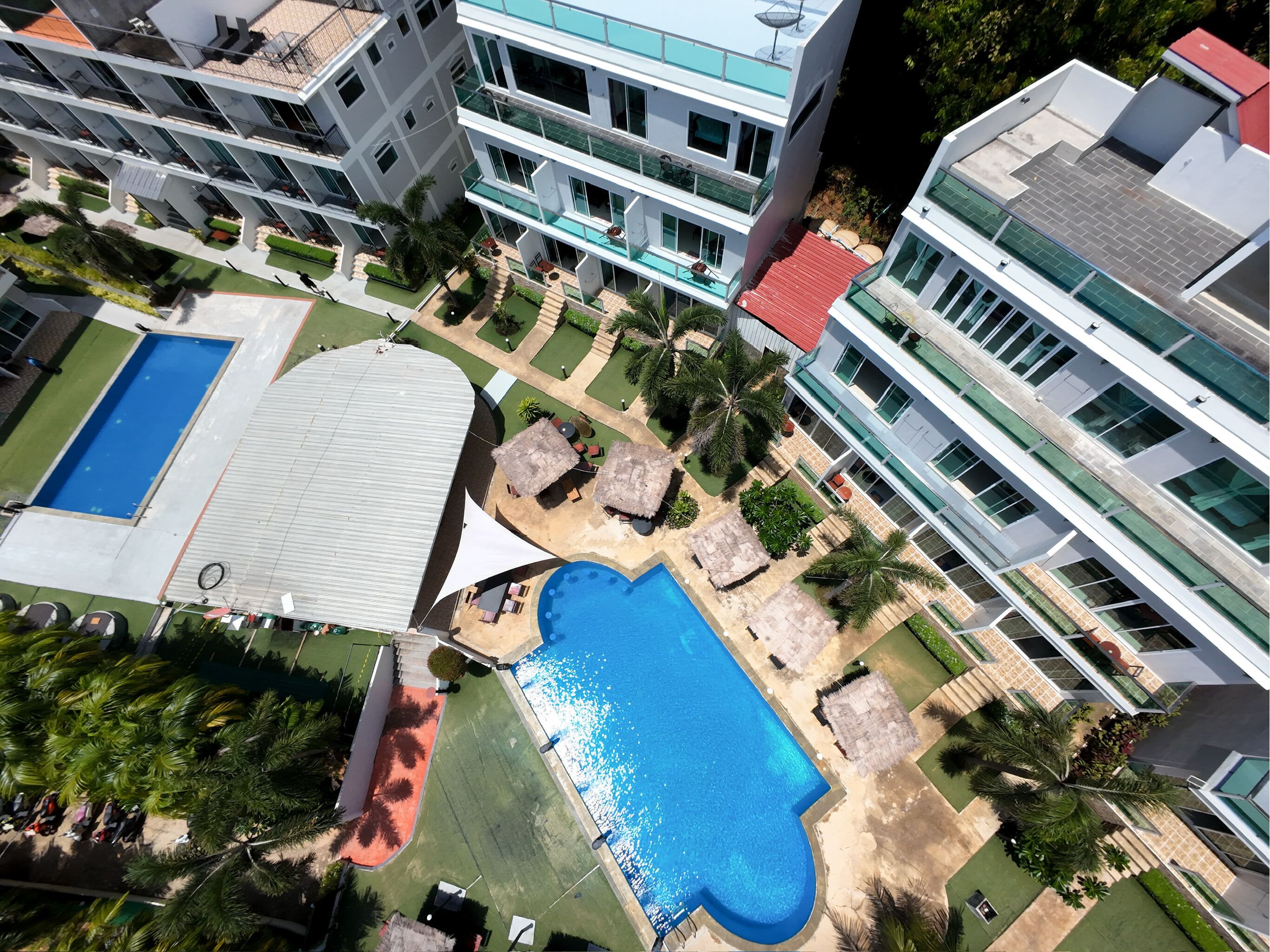 A modern hotel complex with multiple floors, a swimming pool, and a well-maintained garden area.