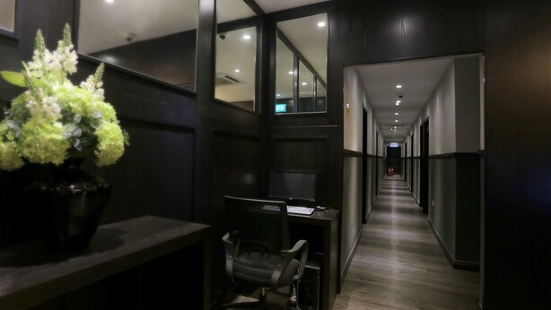 A hallway with a desk and chair, a potted plant, and a long corridor with doors. - Vio Hotel (Kuala Lumpur)