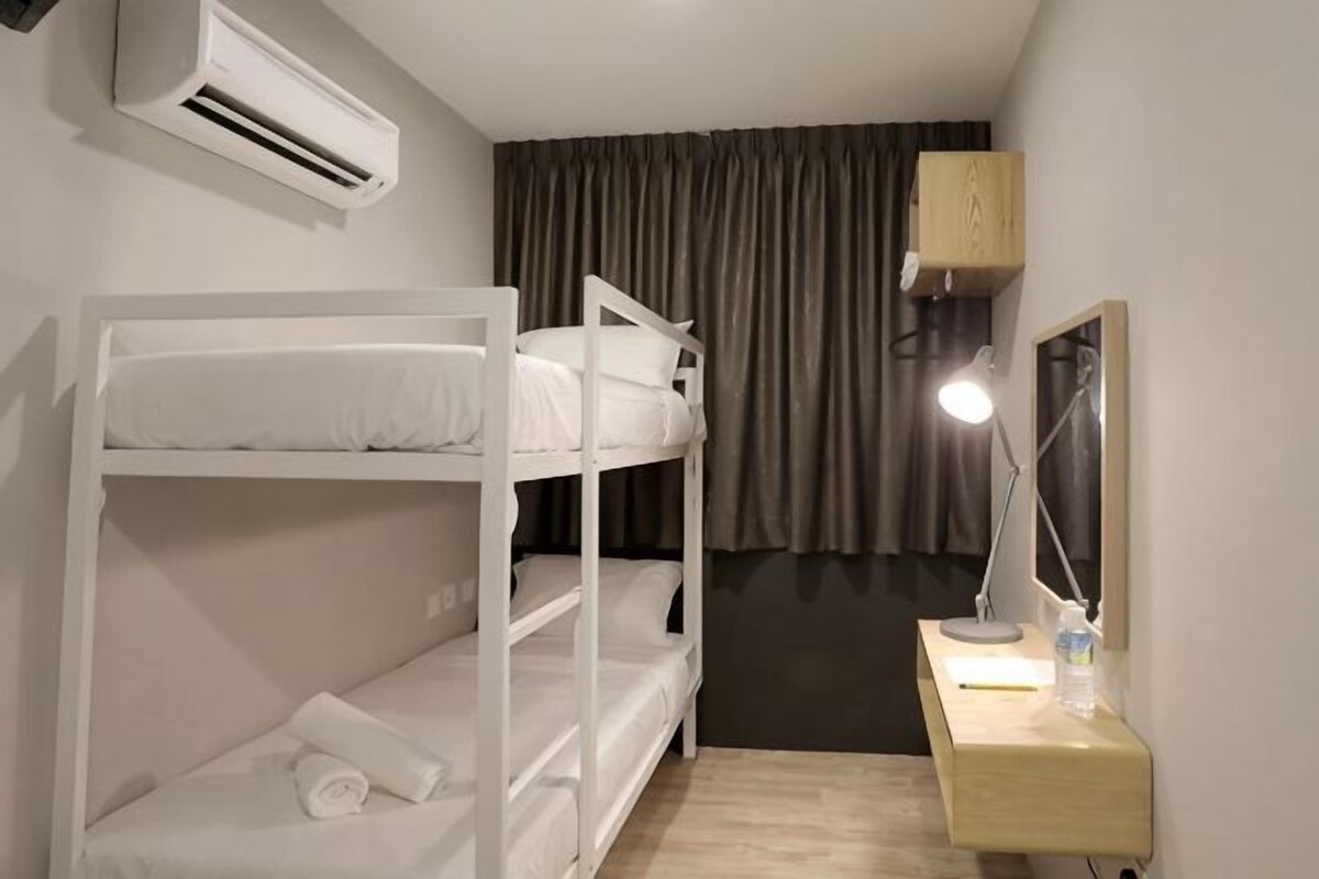 A bunk bed with a flat bed below, a desk with a lamp, a mirror, and an air conditioning unit.