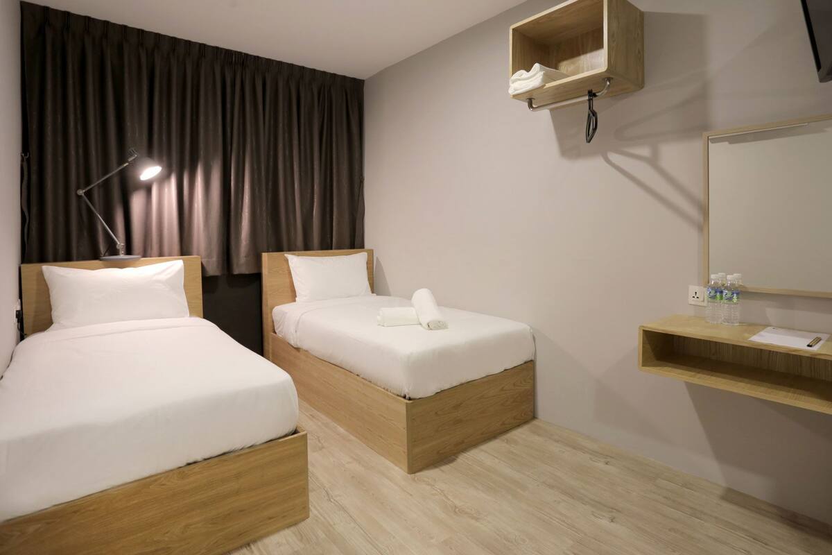 A hotel room with two beds, a desk with a mirror, a shelf with toiletries, and a hanging light.