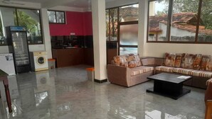 Uma sala de estar ampla com um conjunto de sofás, uma mesa de centro e uma cozinha ao fundo.