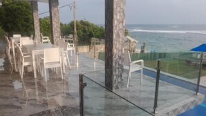 Uma área de estar ao ar livre com cadeiras e mesas brancas, com vista para o oceano.