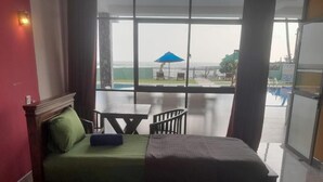Quarto de hotel com duas camas, uma mesinha e vista para a área da piscina.