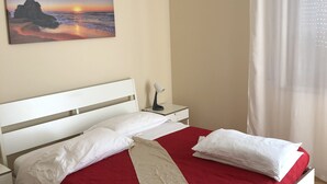 A neatly made bed with a red and white bedspread, a white headboard, and a nightstand with a lamp. - Moon River (Pescara)