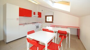 A compact kitchen with white cabinets and red accents, a dining area with a white table and red chairs, and a skylight above the kitchen. - Moon River (Pescara)