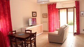 A living room with a sofa, a dining table with chairs, a TV on a cabinet, and a window with curtains. - Moon River (Pescara)