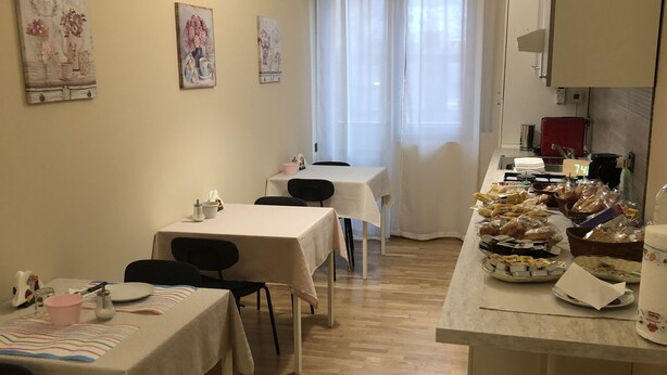 A dining area with tables set for a meal, a kitchen area with food items, and a window with curtains. - Moon River (Pescara)