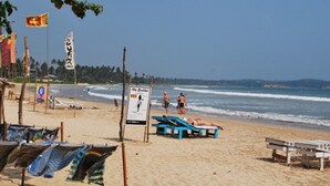 Une plage avec des chaises longues bleues, un panneau indicateur et des drapeaux.