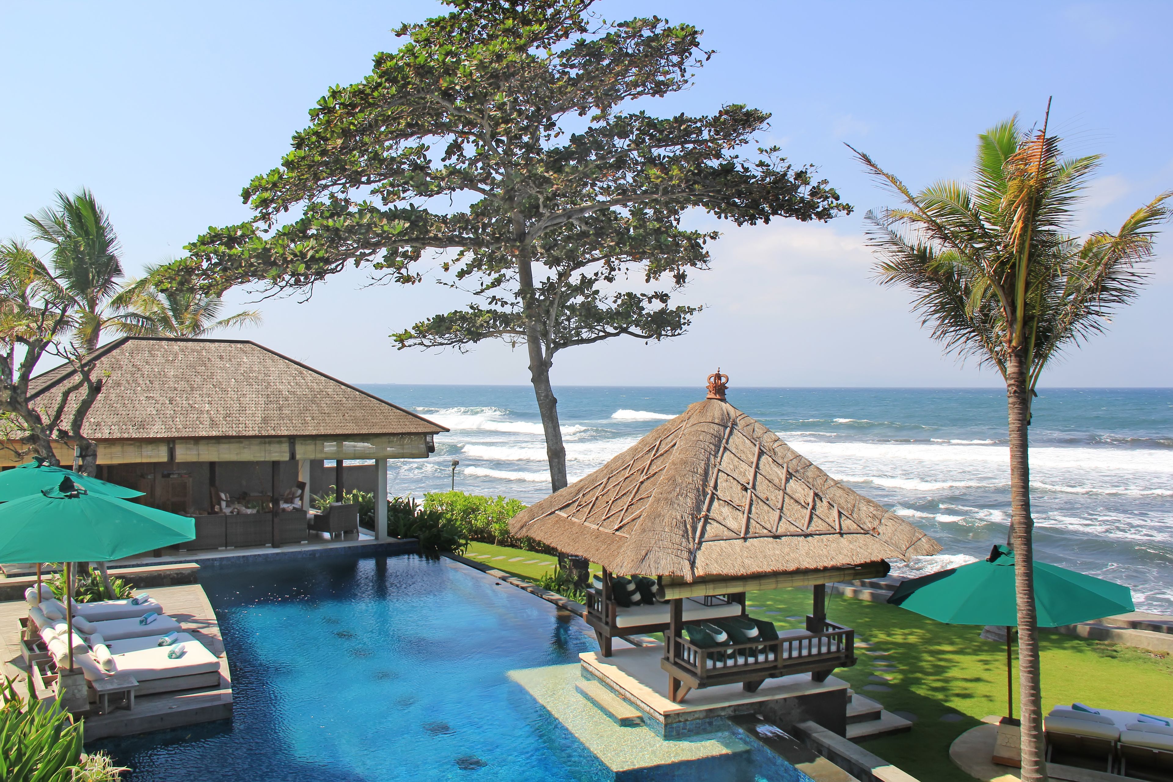 A pool area with lounge chairs and umbrellas, a thatched-roof structure, and a view of the ocean.