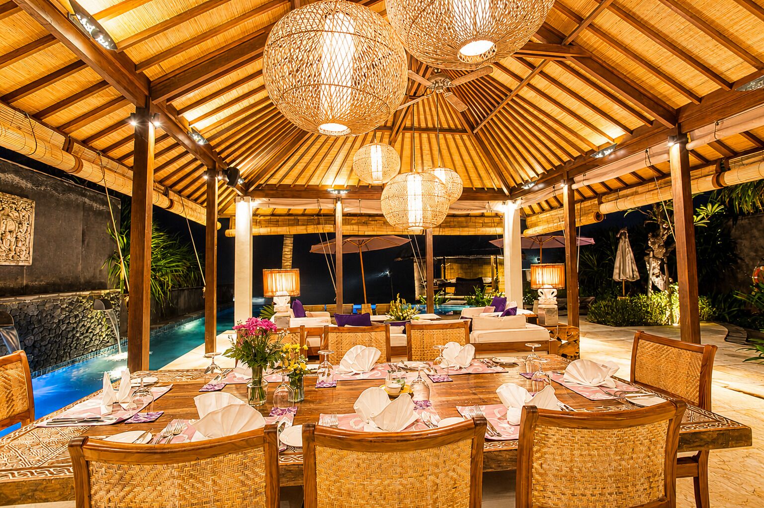 An outdoor dining area with a pool, bamboo ceiling, and wicker furniture.
