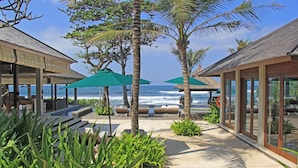 Un resort frente a la playa con terraza al aire libre, palmeras y vistas al océano.