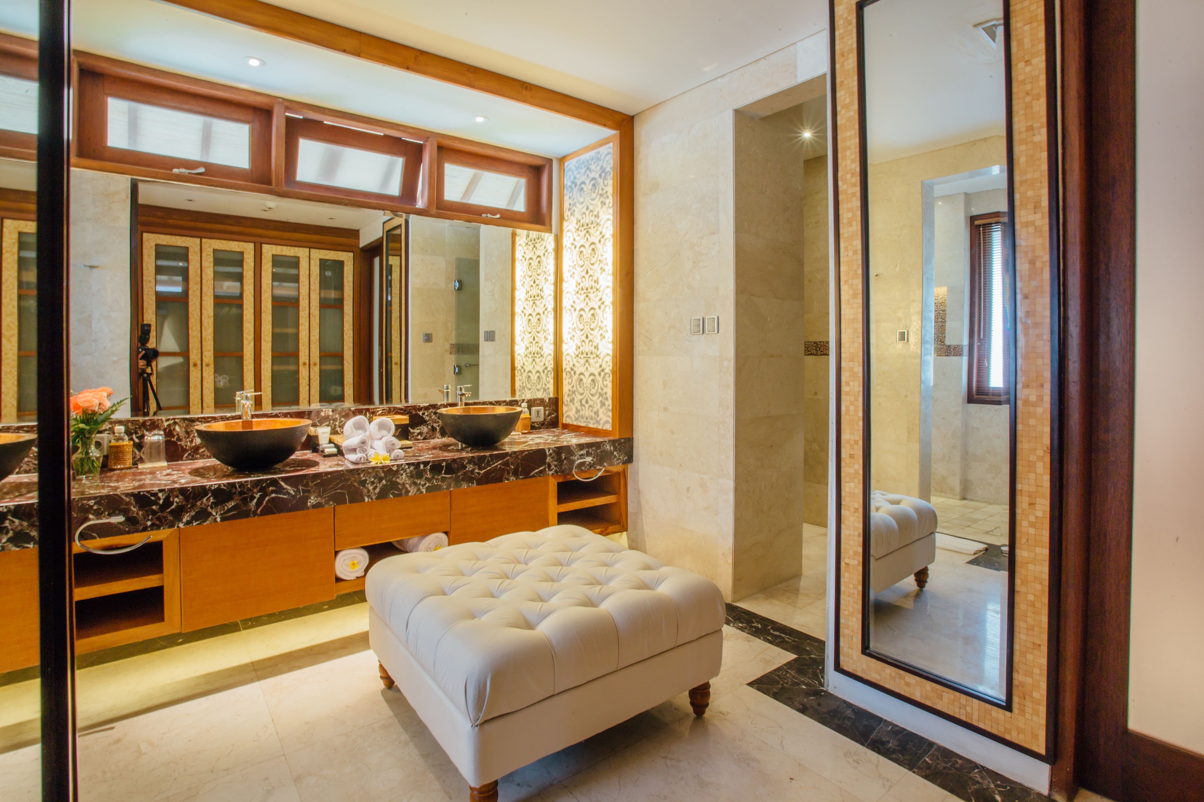 A modern bathroom with a large mirror, dual sinks, a vanity, and a cushioned bench.