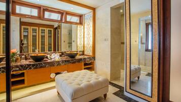 A modern bathroom with a large mirror, dual sinks, a vanity, and a cushioned bench.