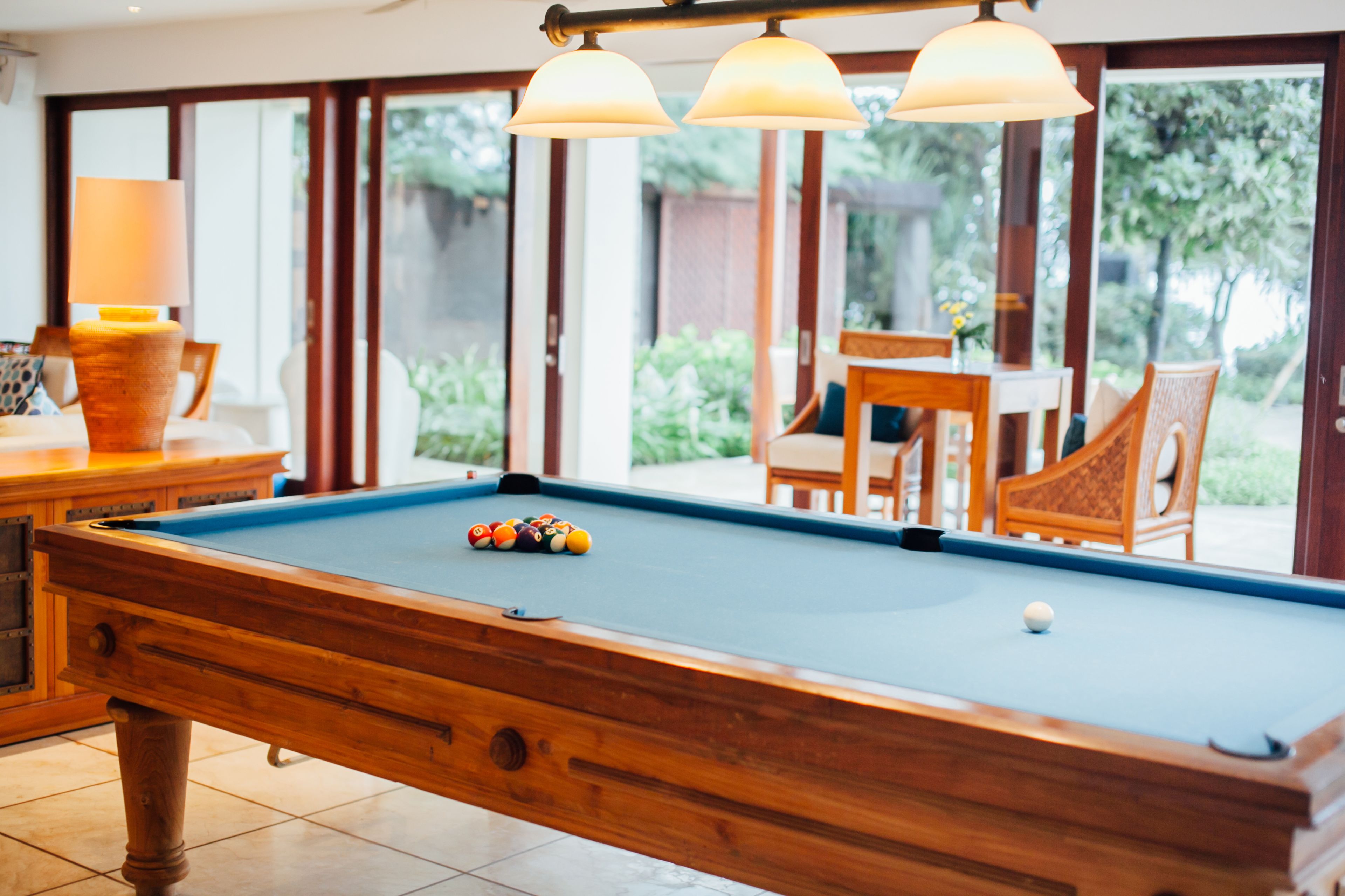 A pool table with balls, a lamp, and a view of an outdoor patio with chairs and a table.