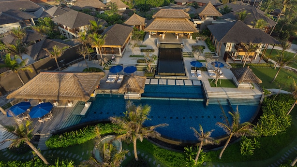Un resort con piscina central, varias habitaciones de huéspedes y palmeras.