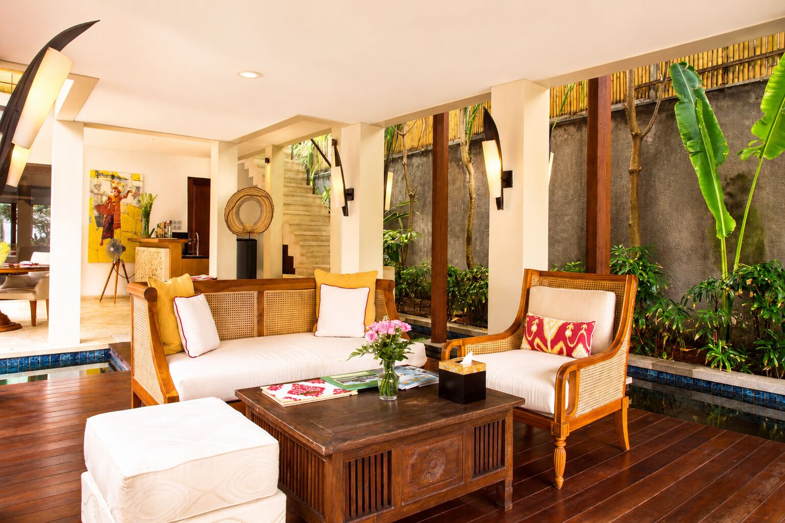 A spacious living area with a sofa, armchairs, and a coffee table, featuring a large window with a view of a water feature and greenery.