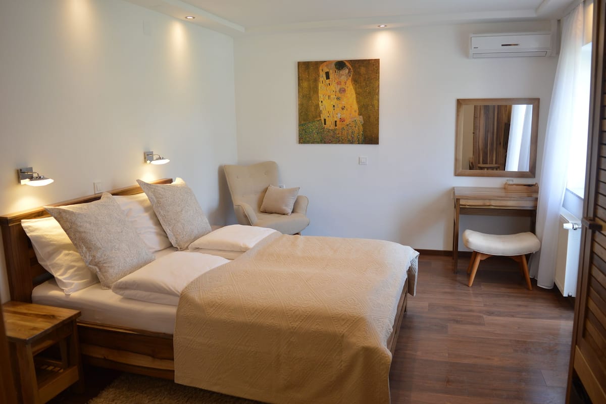 A bedroom with a bed, bedside tables, a chair, a desk, and a painting on the wall.