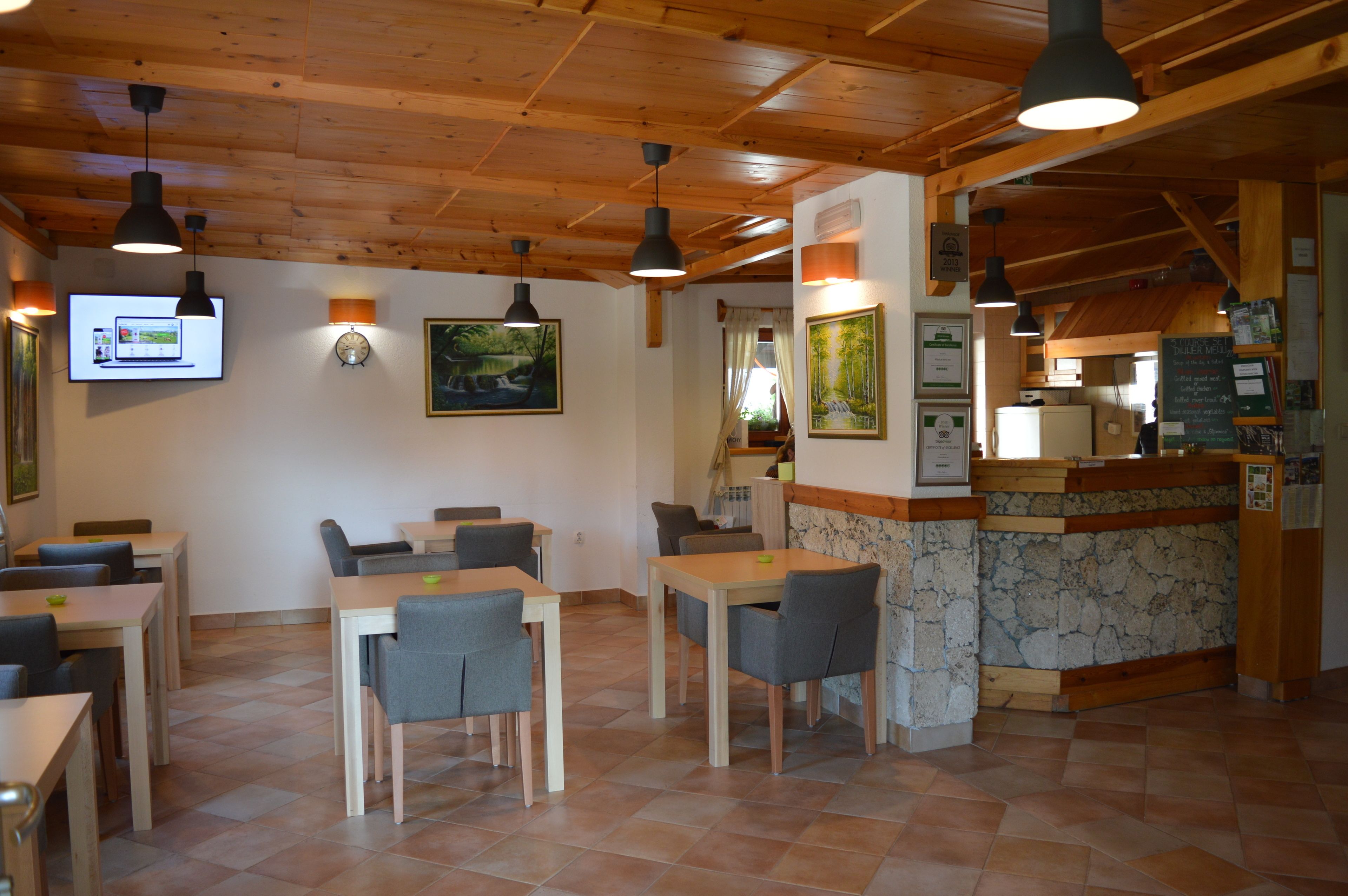 A restaurant with wooden ceiling beams, tables with chairs, a counter with a menu, and wall-mounted artwork.