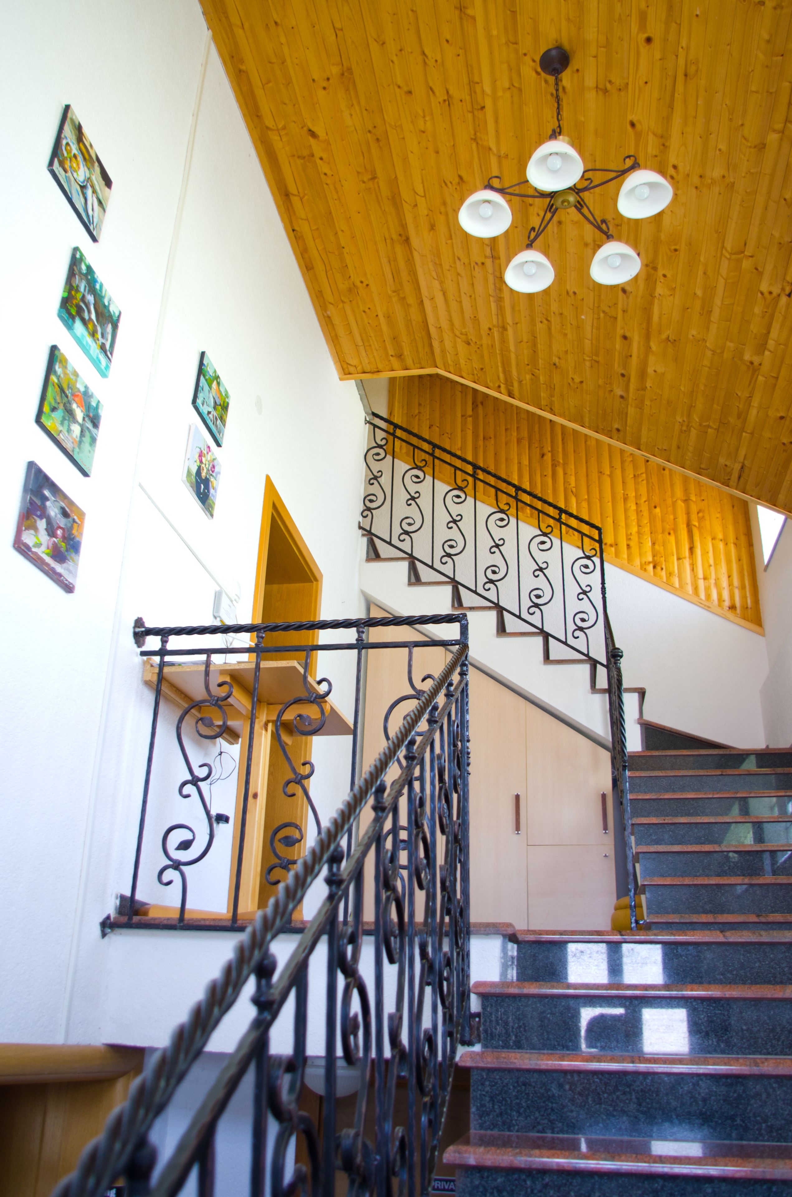 A staircase with ornate metal railings, wooden ceiling, and wall-mounted artwork.