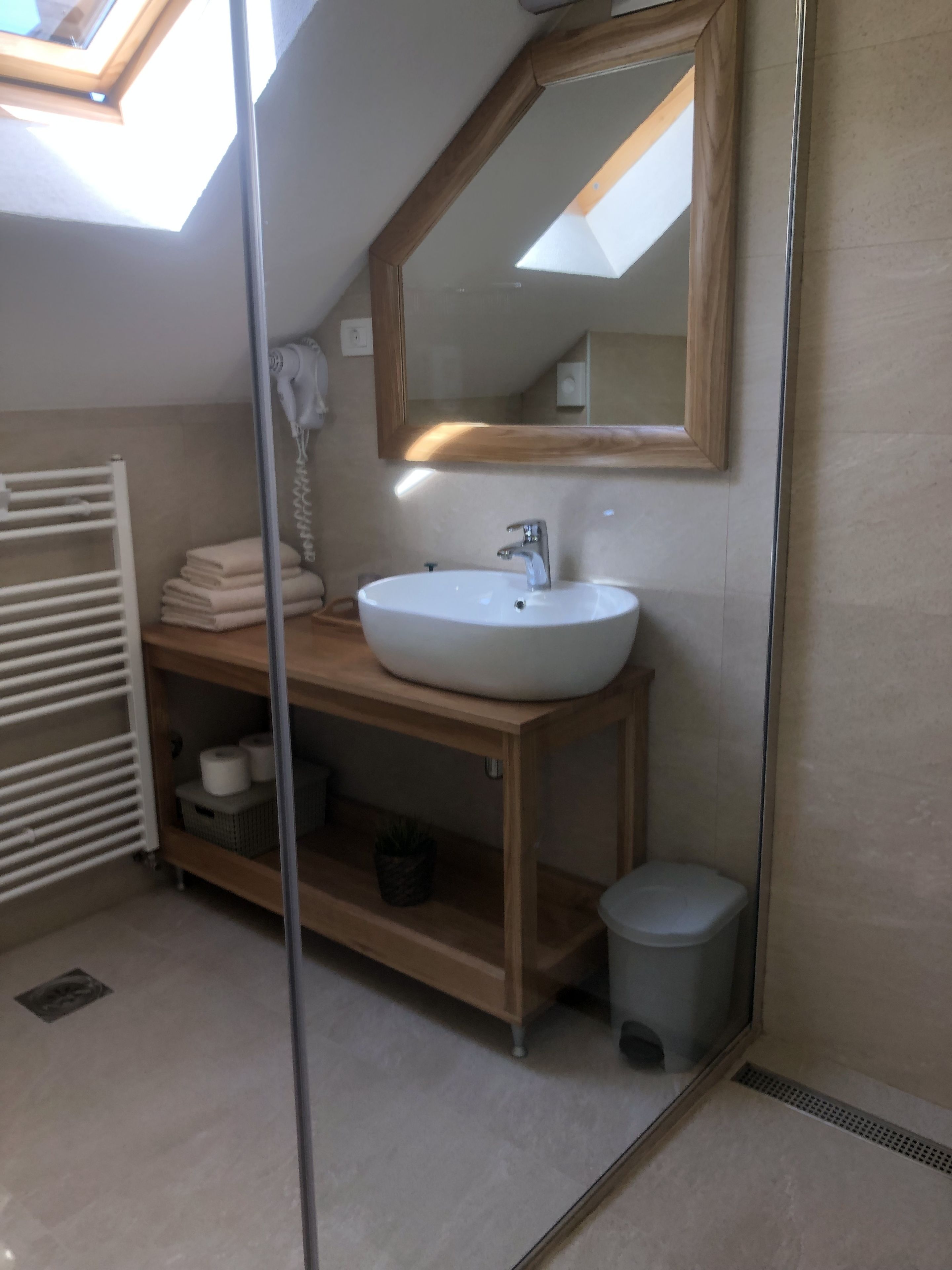 Een moderne badkamer met dakraam, een witte wastafel, een houten wastafelmeubel en een spiegel.