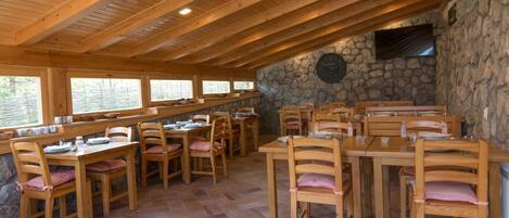 Un restaurante con mesas y sillas de madera, paredes de piedra y un reloj en la pared.