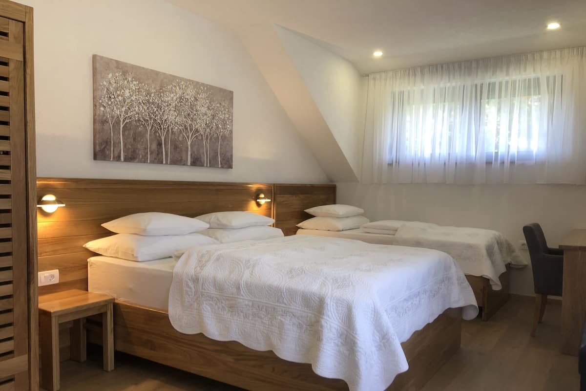 A hotel room with two beds, a wooden headboard, a bedside table, a chair, a desk, and a painting on the wall.