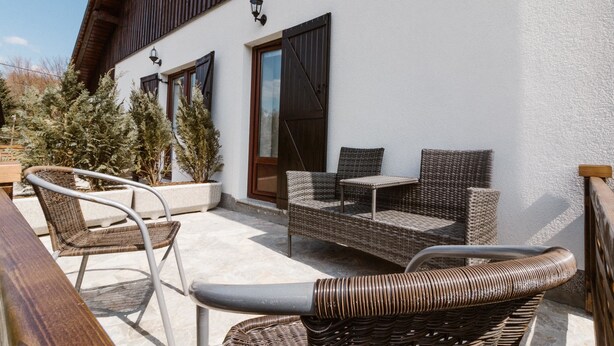An outdoor seating area with wicker furniture and a wooden table, a white building with wooden shutters, and a potted plant. - Plitvice Miric Inn (Plitvicka Jezera)