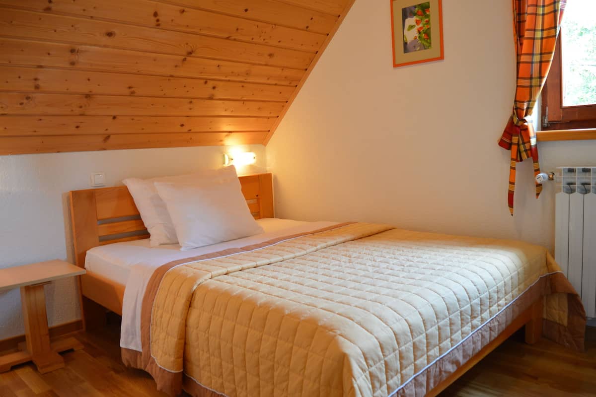 A cozy bedroom with a wooden ceiling, a bed with a quilted blanket, a bedside table, and a window with curtains.