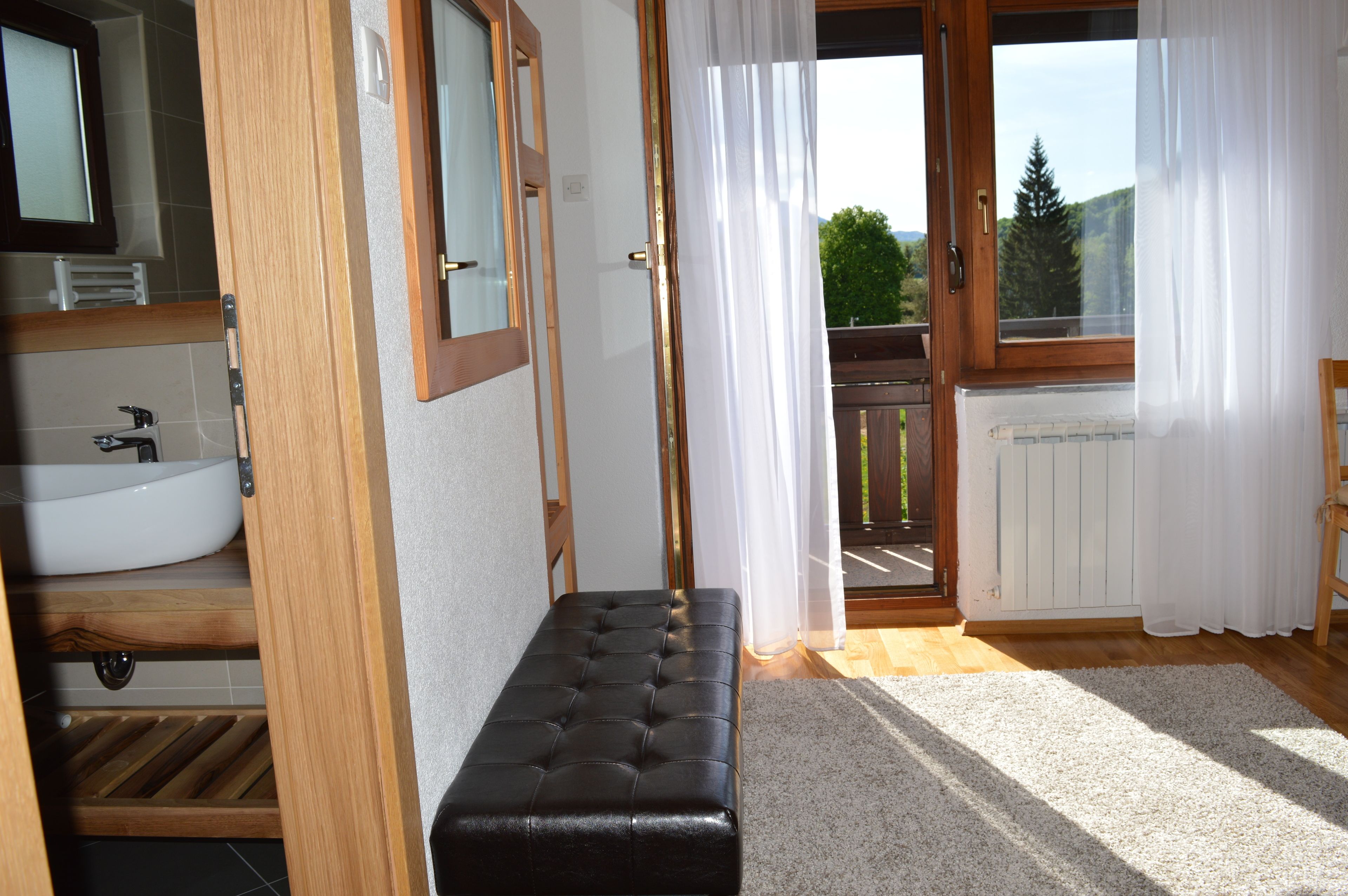 A bathroom with a white sink, wooden bench, and a view of a balcony through a glass door.