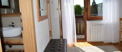 A bathroom with a white sink, wooden bench, and a view of a balcony through a glass door.