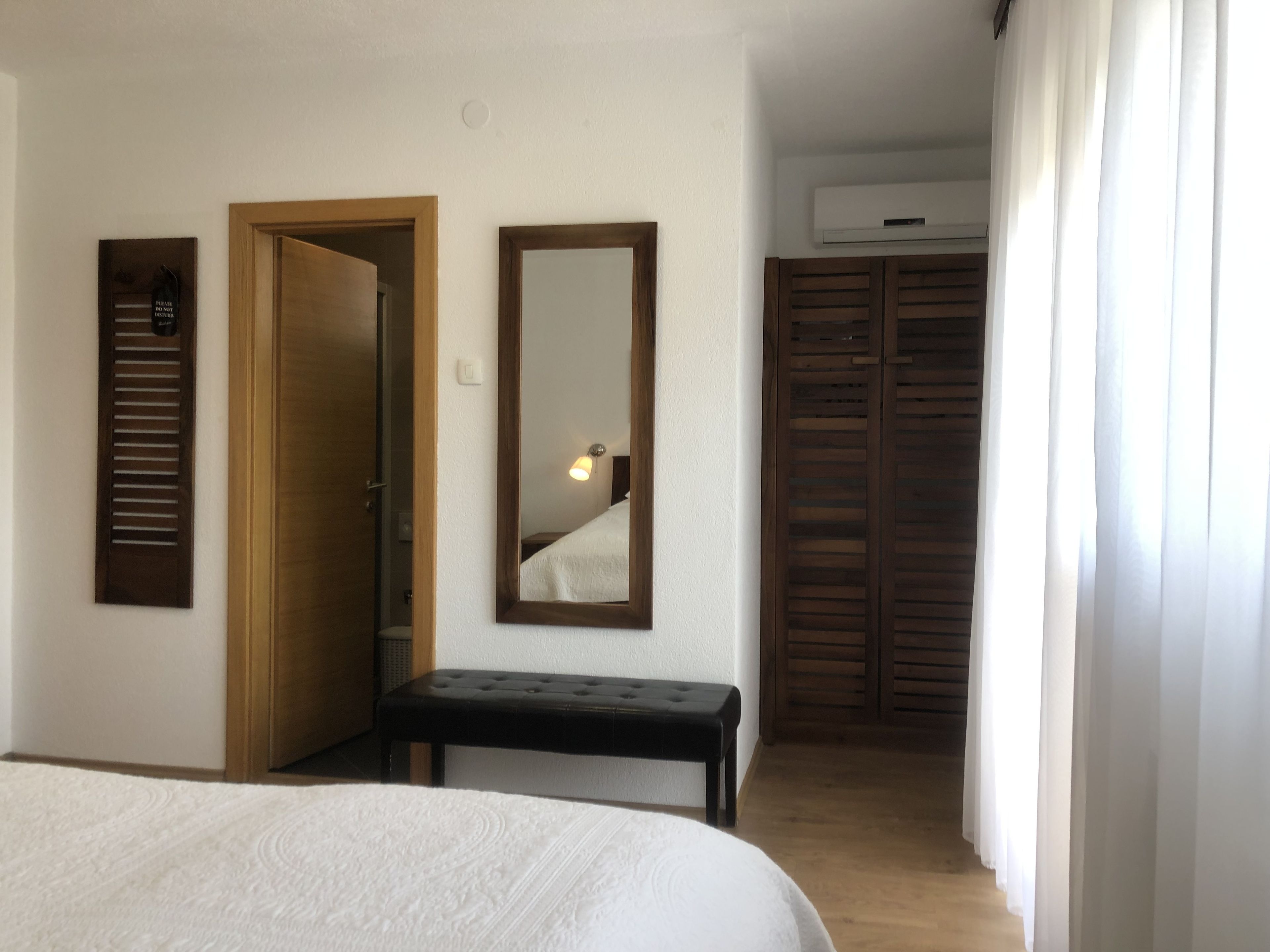Un dormitorio con cama, un banco, un espejo, una puerta y un armario.